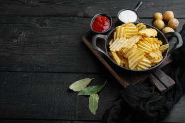 Çıtır patates cipsi. Patates dilimleri, deniz tuzu setiyle kavrulmuş, siyah ahşap arka planda, metin için kopyalama alanı ile birlikte.