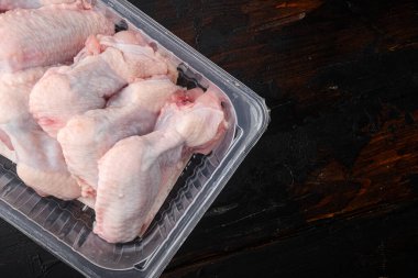 Fresh chicken wings spit in plastic vacuum pack set, on old dark  wooden table background, top view flat lay, with copy space for text