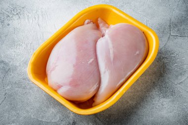 Çiğ tavuk göğsü filetoları tepside, gri arka planda.