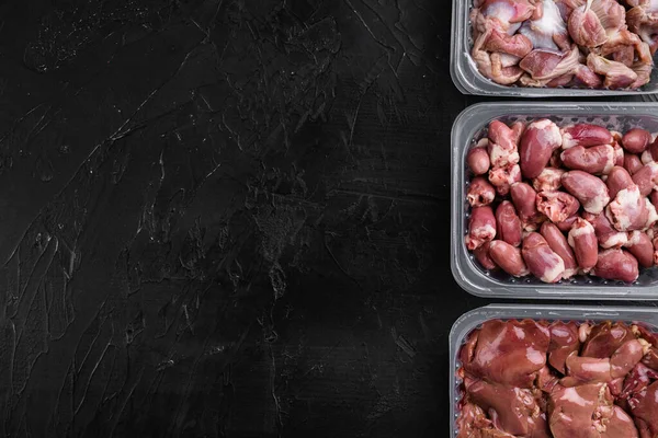 Raw uncooked Bird chicken giblets gizzards, stomachs, liver, offal, hearts set, on black dark stone table background, top view flat lay, with copy space for text