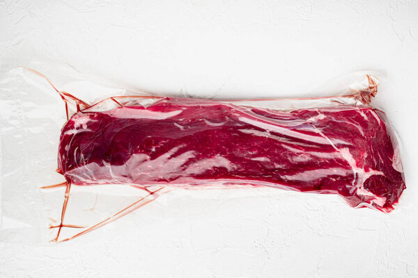 Raw beef tenderloin marbled meat in plastic pack set, on white stone  background, top view flat lay