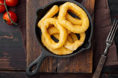 Kızarmış kalamar halkaları. Kızarmış deniz ürünleri seti dökme demir tavada tavada, eski koyu ahşap masa zemininde, üst manzara düz yatıyordu.