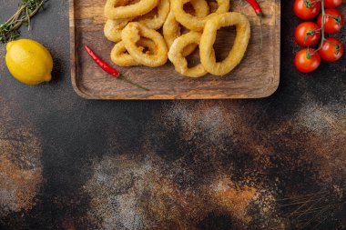 Kızarmış mürekkep balığı halkaları servis panosunda, eski koyu kırsal masa zemininde, üst görünüm düz yatağında, metin alanı için kopyalama alanı ile birlikte.