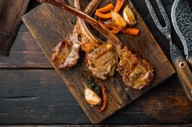 Izgara kuzu kaburga fileto seti, ahşap servis tahtasının üzerinde, eski koyu ahşap masa zemininde, telif yeri ve metin için yeri olan üst manzara düz yerde.