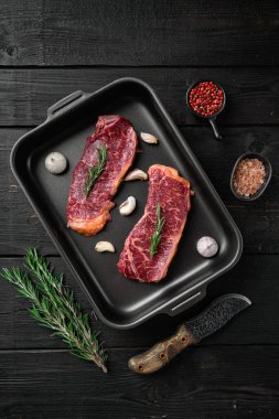 Çiğ et New York bifteği ve baharat seti, siyah ahşap masa arka planı, üst manzara düz yatıyordu