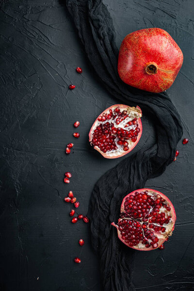 Ripe pomegranate with juicy seeds, on black textured background, flat lay with space for text