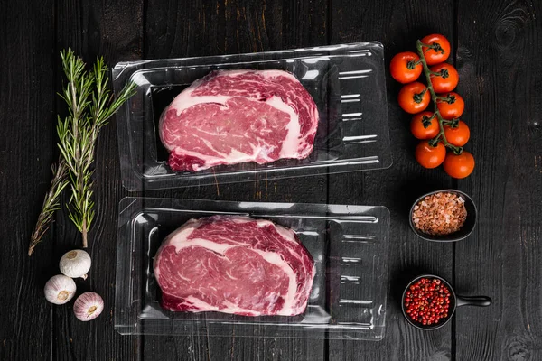 Vacuum sealed meat cut set, on black wooden table background, top view flat lay