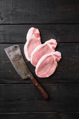 Çiğ domuz bifteği, otlarla pişirmeye hazır, siyah ahşap masa arkaplanında, en üstteki düz görünümde, metin alanı için fotokopi alanı ile