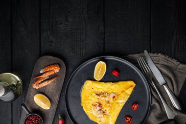 İspanyol omleti, taze kırmızı biber, kahverengi ve beyaz yengeç eti, limon, Çedar peyniri, kızarmış yumurta, tabakta, siyah ahşap masa zemininde, en üstte düz görünüm, metin için yer ve mekan.