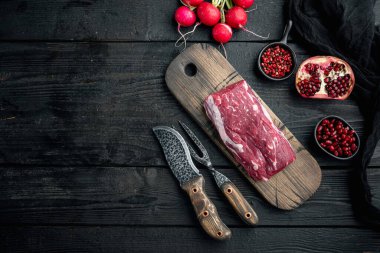 Çiğ sığır fileto bifteği, otlu ve baharatlı bonfile fileto seti, dökme demir kızartma tavasında, siyah ahşap masa zemininde, düz görünüm yatağı, metin için kopya alanı