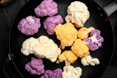 Karnabahar çeşitleri. Mor, sarı ve beyaz set, kızgın demir tavada, siyah ahşap masa zemininde, üst manzara düz