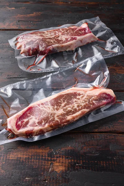 Vacuum packed meat , top blade beef steak on dark old wooden table,  side view selective focus