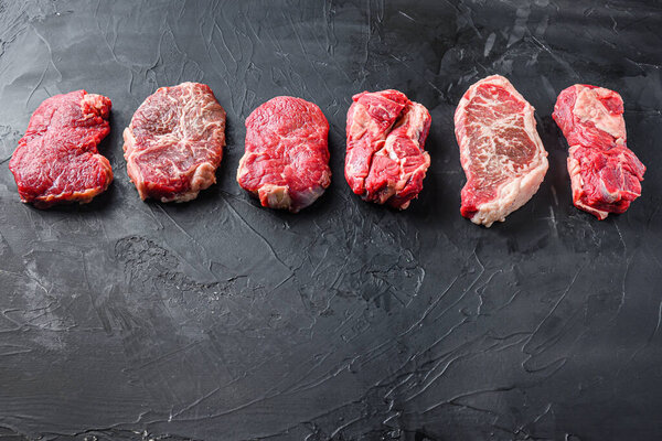 Raw set of rump, top blade, chuck roll beef steak cut, on black textured background, side view with space for text