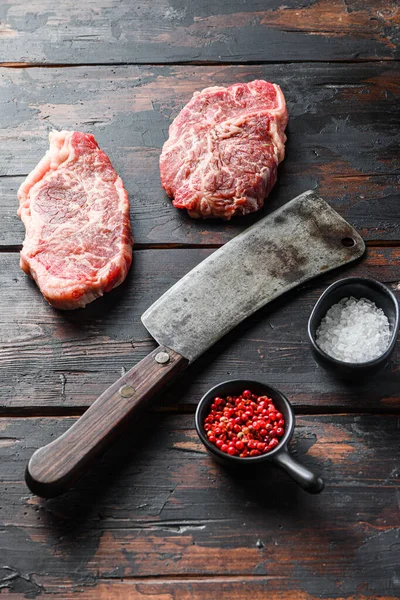 Top blade organic meat cut, raw marbled beef steak, with old butcher knife cleaver and seasonings  On dark wooden rustic table, side view