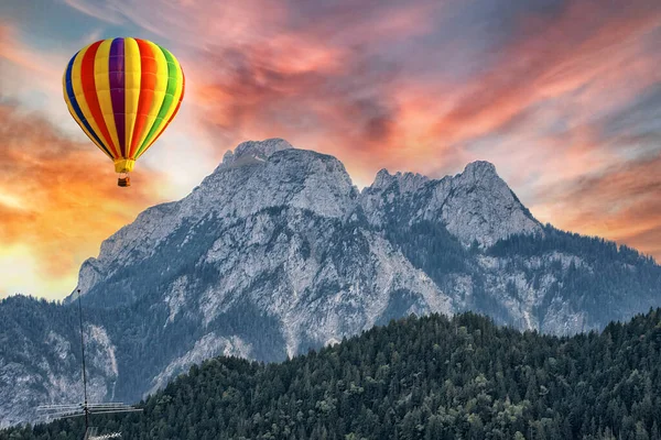 高阿尔卑斯山背景下的热气球在明亮的落日的天空下掠过青翠的森林 — 图库照片