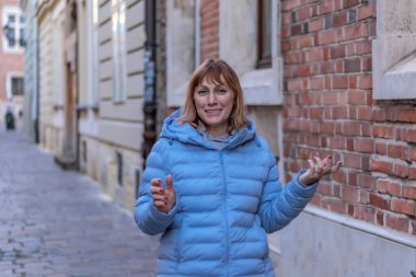 Güzel kızıl saçlı, 50 yaşında bir kadın, orta yaşlı, eski tuğladan evlerle sokakta yürüyor.