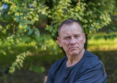 Erkek portresi, yakışıklı, olgun, düşünceli, seksi bir adam, yeşil arka planda bir parkta oturuyor.