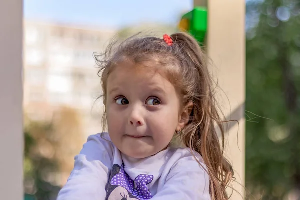 5岁的欧洲小女孩 一头棕色的长发 一双大大的褐色眼睛 坐在公园里 脸上带着一张狡猾的脸 一张学龄前儿童的特写 在街上 — 图库照片
