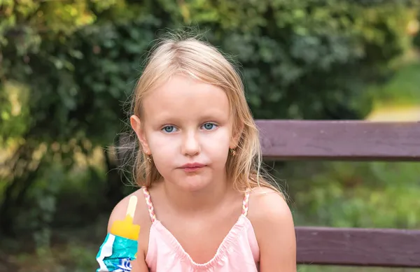 7岁的金发小女孩 满脸愁容 坐在公园的长椅上 吃着爆米花 这是一个吃冰淇淋的孩子的画像 — 图库照片