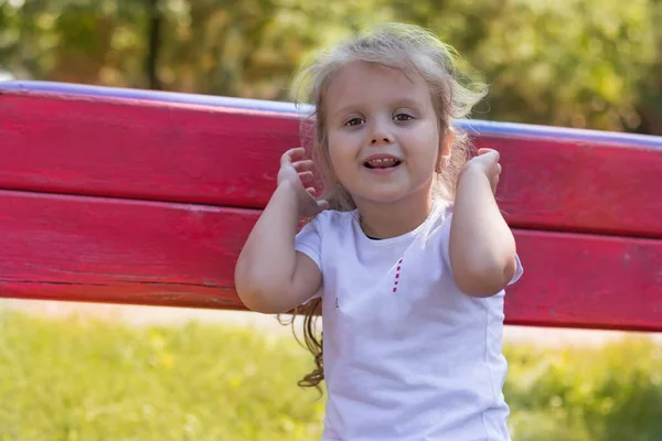 有趣的女孩4岁的金发女郎坐在长椅上 举起双手笑了 — 图库照片
