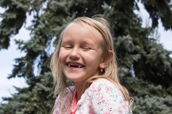 一个快乐的小女孩 金发碧眼 没有门牙 心情很好 在公园的冷杉树前开怀大笑 — 图库照片