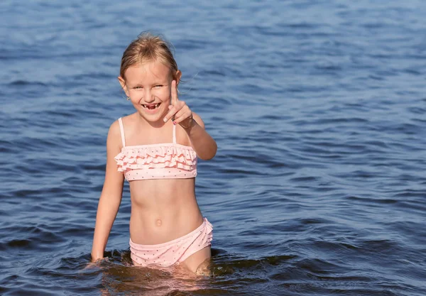 6歳から7歳の少女はピンクの水着姿で海の水の中に立ち青い海を背景に子供の肖像画を描き ストック画像