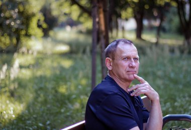 Yakışıklı, olgun orta yaşlı bir adamın portresi. Parktaki bankta oturuyor.