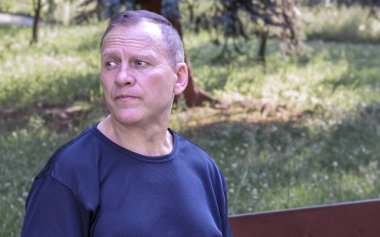 Yakışıklı, olgun orta yaşlı bir adamın portresi. Parktaki bankta oturuyor.