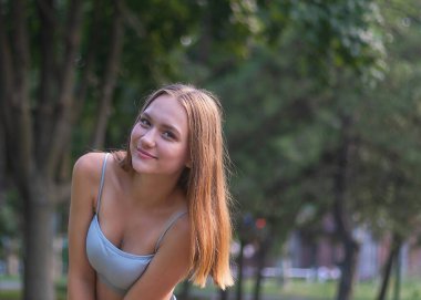Güzel genç bir kız, narin ve çekici, 16 yaşında, uzun saçlı, parkta oturuyor.
