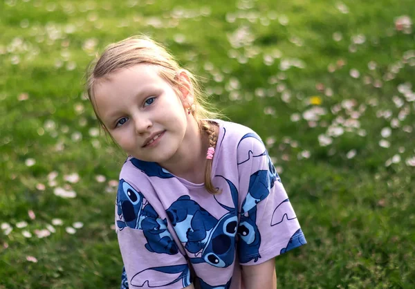ヨーロッパのブロンドの女の子の肖像7歳緑の花の牧草地に座って ロイヤリティフリーのストック画像