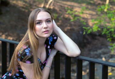 16 yaşında, uzun saçlı, yaz elbisesi giyen güzel bir kız parkta oturuyor.