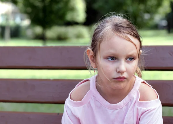 7歳のブロンドの女の子はベンチの公園で深刻な顔をして悲しい目をしています — ストック写真