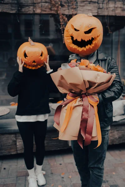 The guy gives his girlfriend a bouquet, both with a pumpkin head — Stock Photo, Image