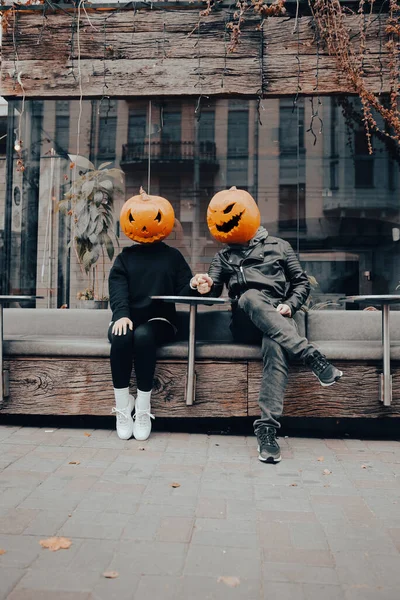 Guy and girl with pumpkin heads in a street cafe holding hands — Stock Photo, Image