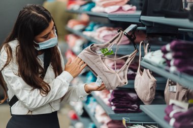 Mağazadaki kız tıbbi maske takıyor, iç çamaşırı seçiyor.