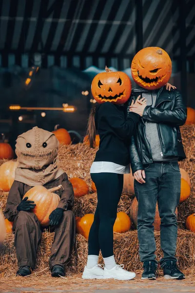 A guy and a girl with a pumpkin heads posing at the scarecrow — Stock Photo, Image