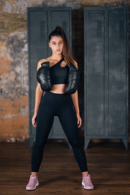 Spor giyimli bir kadın boks eldivenleriyle kameraya poz veriyor..