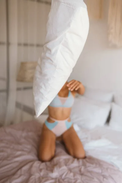 Женщина в нижнем белье играет с подушкой на кровати — стоковое фото
