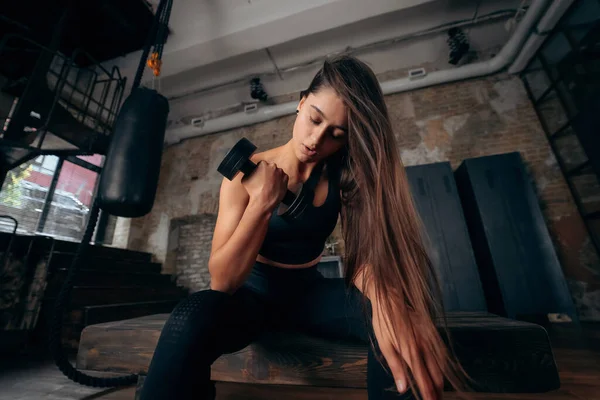 Mujer joven bombea los músculos por un brazo levantando la mancuerna. — Foto de Stock