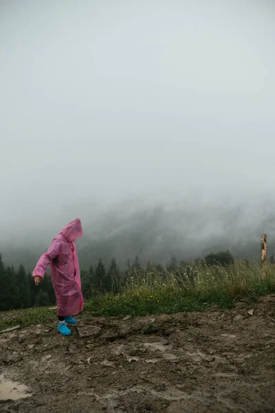 Atractiva chica excursionista en un impermeable rosa se encuentra en una montaña — Foto de Stock
