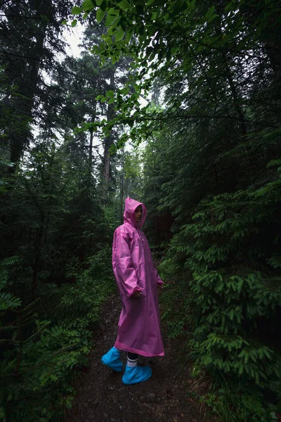 Ung kvinne i regnfrakk går gjennom skogen i regnet. – stockfoto