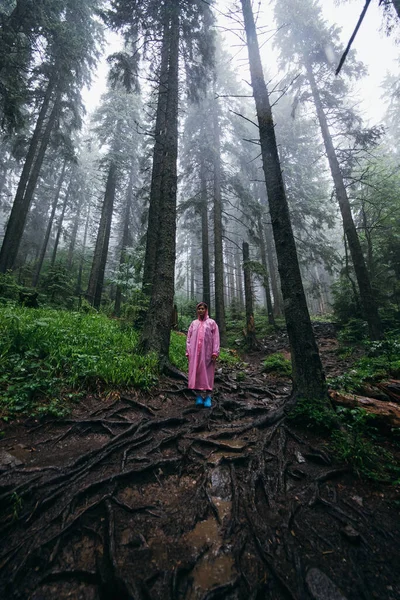 Ung kvinna i regnrock går genom skogen i regnet — Stockfoto