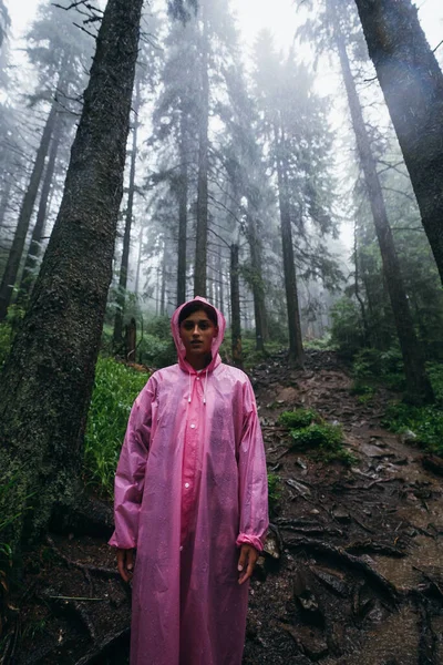 Молода жінка в плащі йде через ліс під дощем — стокове фото