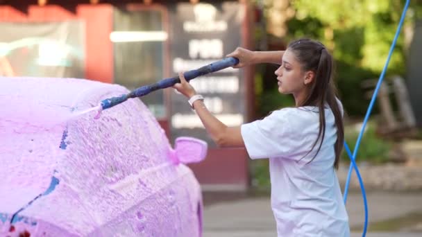 Brunett från en högtrycksslang applicerar en renare på bilen — Stockvideo
