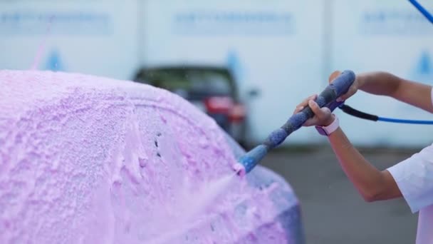Brunette van een hogedrukslang brengt een reiniger aan op de auto — Stockvideo