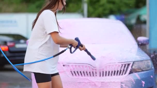 Brunette van een hogedrukslang brengt een reiniger aan op de auto — Stockvideo