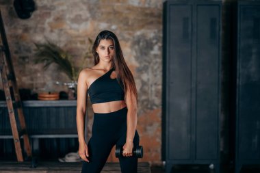 Elinde dambıllarla kameraya poz veren genç bir kadın..