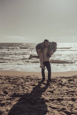 Erkek kız arkadaşını sırtında taşır, çift sahilde eğlenir.