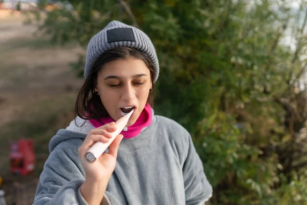 Jovem mulher escovando os dentes com uma escova elétrica na natureza — Fotografia de Stock