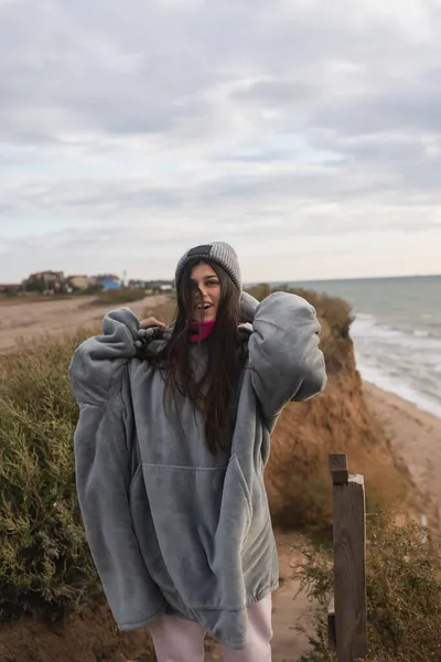 Soğuk sonbahar sahilinde kameraya poz veren genç bir kadın. — Stok fotoğraf